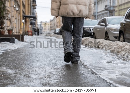 Pedestrian walking on slippery sidewalk rear view. Pavement covered with slippery ice. Frozen rain. Winter time. 
