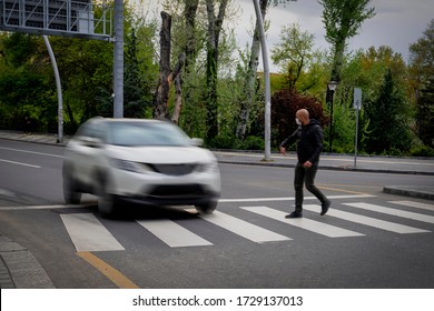 Pedestrian walking on zebra crossing and a driving car failing to stop in blurred motion. Pedestrian reacts with hand to the driver.
				