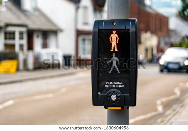 Pedestrian zebra crossing with\
an English text telling people to wait for appropriate signal and\
push the button. The blurred car in the background is approaching\
