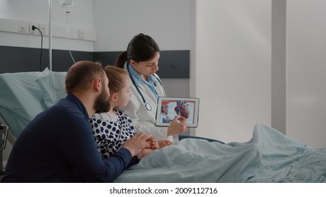 Pediatric Cardiologist Woman Doctor Explaining Heart Illness Using Tablet With Medical Cardiogram On Display During Surgery Consultation In Hospital Ward. Sick Child Recovering After Sickness Surgery