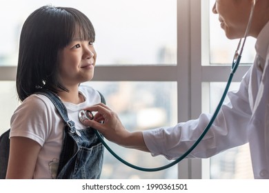 Pediatric Care With Happy Child Patient And Pediatrician Doctor Examining Asian Girl Kid Heart And Lung Health With Stethoscope In Medical Clinic, Healthcare Checkup Service Concept