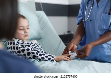 Pediatric Clinic Nurse Measuring Sick Little Girl Oxygen Levels Using Oximeter. Medical Hospital Staff Measuring Ill Young Patient Oxygen Levels Using Oximeter While Resting On Pediatric Clinic Bed.