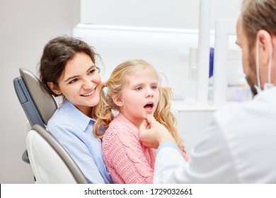 Pediatric dentist examines a frightened child on the lap of a mother or a medical assistant
