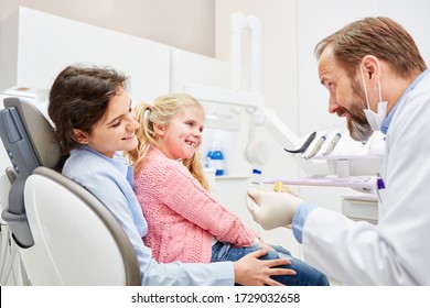 Pediatric dentist explains child on the mother's lap the planned treatment in the doctor's office