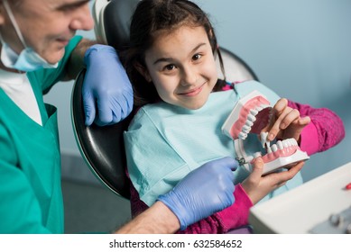 Pediatric dentist showing to girl dental jaw model at dental clinic. Dentistry, early prevention, oral hygiene concept.