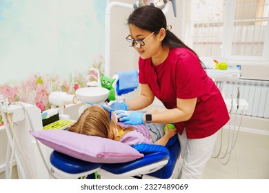 A pediatric dentist treats or performs oral hygiene for a little girl. regular visits to the doctor and prevention of dental diseases. - Powered by Shutterstock