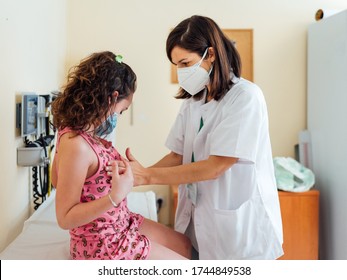 Pediatric Doctor Examines A Sick Child With A Face Mask For The Virus.Sick Girl Is Checked At The Clinic For A Medical Diagnosis.Pandemic Covid19 And Coronavirus.the Girl Sitting On The Hospital Bed.