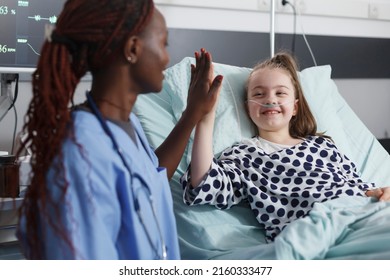 Pediatric Hospital Nurse Highfive Sick Child While In Patient Treatment Ward Room. Blessed Cheerful Young Patient Highfive Medical Staff While In Medical Examination Room.