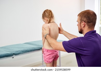 Pediatric Orthopedist Physiotherapist Examining Child's Back In Clinic. Scoliosis Treatment. Vertebrologist Identifies Spinal Problems In Girl. Medicine And Healthcare Concept