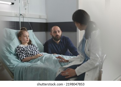 Pediatric therapist discussing with father of hospitalized sick daughter resting in patient bed. Doctor specialist examining ill kid under treatment resting in children healthcare facility ward. - Powered by Shutterstock