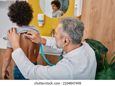 Pediatrician auscultating boy's lungs using a stethoscope while pediatrician consultation at clinic. Curly male child has pneumonia or coronavirus - Powered by Shutterstock