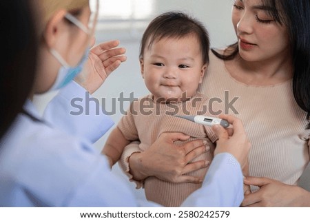 Pediatrician checking baby temperature with thermometer in clinic.