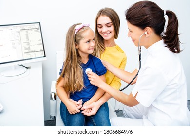 Pediatrician check-up the child's lungs and heart using a phonendoscope. Little girl sitting on mother's arms while medical exam in hospital