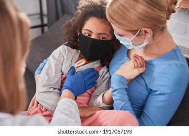 Pediatrician With Child Patient In Room Interior. Curly Multiracial Girl Wearing Protective Mask And Her Blonde Caucasian Mom At Doctor Appointment For Health Checkup. Doctor Visit Concept