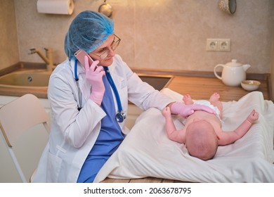 Pediatrician Doctor Calling On The Phone And Newborn Baby. A Nurse In Uniform With A Child Is Consulted By A Mobile Phone