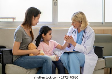 Pediatrician Doctor Examining Little Asian Girl With A Broken Arm Wearing A Cast At Hospital