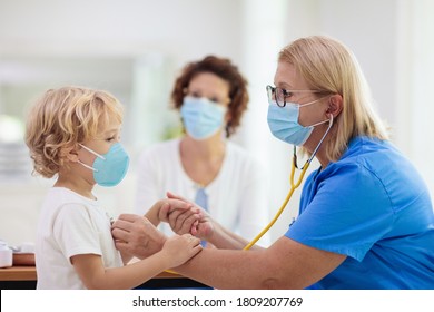 Pediatrician Doctor Examining Sick Child In Face Mask. Ill Boy In Health Clinic For Test And Screening. Kids Home Treatment Of Virus. Coronavirus Pandemic. Covid-19 Outbreak. Patient Coughing.