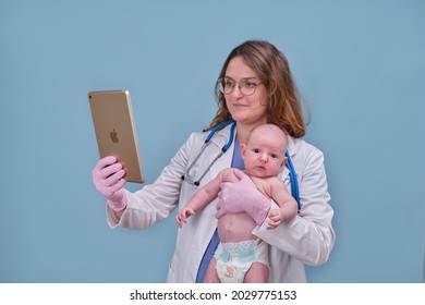 Pediatrician Doctor Holding Apple Ipad And Newborn Baby, Blue Studio Background. Happy Nurse In Uniform With Baby And Digital Tablet - Moscow, Russia, August 12, 2021