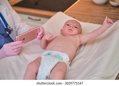 Pediatrician Doctor Holding IPhone Apple And Newborn Baby. Nurse In Uniform With A Child And A Mobile Phone - Moscow, Russia, August 17, 2021