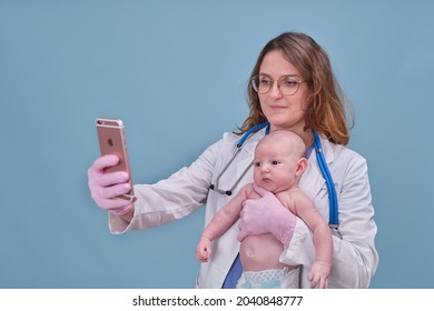 Pediatrician Doctor Holding IPhone Apple And Newborn Baby, Blue Studio Background. Happy Nurse In Uniform With A Child And A Mobile Phone - Moscow, Russia, August 12, 2021