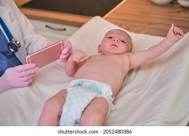 Pediatrician Doctor Holding Phone And Newborn Baby. Happy Nurse In Uniform With A Child And A Mobile Phone