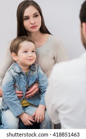 Pediatrician Doctor Holds Tablet Pc Examining Child And Consulting His Mother.