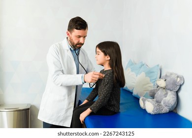 Pediatrician doctor listening to the heartbeat and breathing of a young girl during a medical exam - Powered by Shutterstock