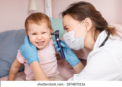 Pediatrician Examines Ear Of Baby Girl At Home During Coronavirus COVID-19 Pandemic Quarantine. Doctor Using Otoscope (auriscope) To Check Ear Canal And Eardrum Membrane Of A Child