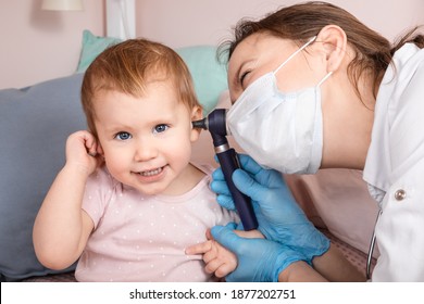 Pediatrician examines ear of baby girl at home during coronavirus COVID-19 pandemic quarantine. Doctor using otoscope (auriscope) to check ear canal and eardrum membrane of a child