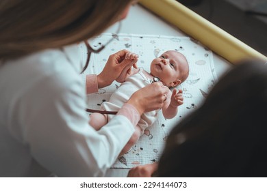 Pediatrician examining cute baby in clinic. Baby lying on her back and is looking up to the pediatrician who is listening her heart. Doctor pediatrician and baby patient - Shutterstock ID 2294144073