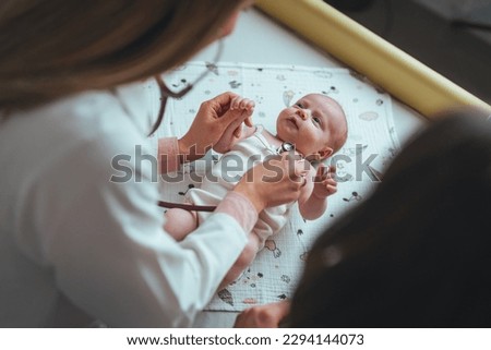 Pediatrician examining cute baby in clinic. Baby lying on her back and is looking up to the pediatrician who is listening her heart. Doctor pediatrician and baby patient