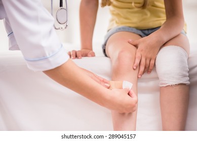 Pediatrician Female Doctor Bandaging Child's Leg. Close-up.