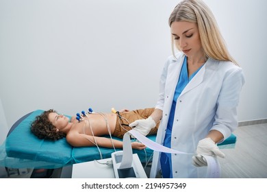 Pediatrician Looking ECG Printout Of Child Patient After Heart Electrocardiogram Procedure At Medical Clinic