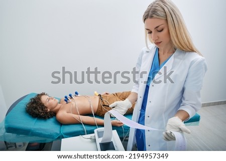 Pediatrician looking ECG printout of child patient after heart electrocardiogram procedure at medical clinic
