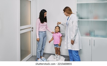 Pediatrician measures Asian female child's height during visit of child with her mother to medical clinic for consultation. Pediatrics - Powered by Shutterstock