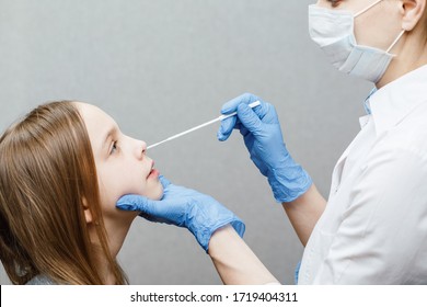 Pediatrician taking nasal mucus test sample from elementary age girl's nose performing respiratory virus testing procedure