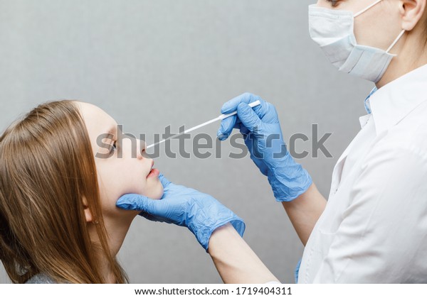 Pediatrician taking nasal mucus test sample\
from elementary age girl\'s nose performing respiratory virus\
testing procedure