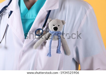 Pediatrician with toy bear and stethoscope on yellow background, closeup