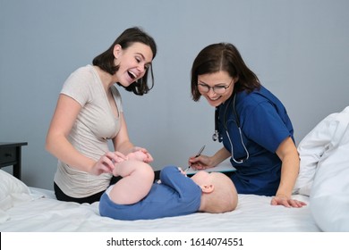 Pediatrician Woman Doctor In Blue Uniform With Stethoscope Talking To Young Mother Of Little Boy, Examining 7 Month Old Baby At Home. Pediatrics, Care And Health Of Children Up To One Year