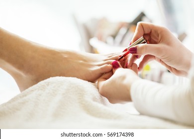 Pedicure in beauty salon. Nail polishing with red nail polish. Close up.