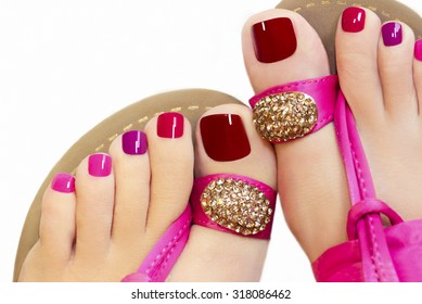 Pedicure with different colors of paint on a woman's feet in pink sandals on a white background.