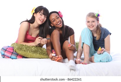 Pedicure fun at pyjama party for three teenage girl friends, a mixed race african american, oriental Japanese and blonde caucasian school mates all wearing flower or feather hair accessories.