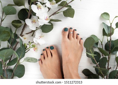pedicure with green nails on a white wooden background with leaves and orchids