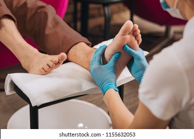 Pedicure for guy. Close up of female hands massaging male foot while woman working at nail bar