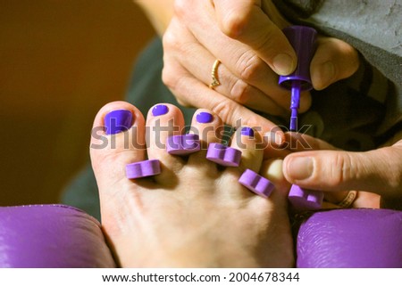 Pedicure master applies bright purple nail polish to client's nails in beauty salon. Women's fingers, toe divider up close. Pedicure Accessories. Girl applying nail varnish to toe nails at spa center.