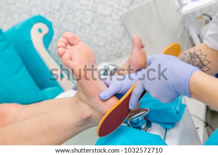 Pedicure master during work. Closeup of female feet and hands in gloves with a nail file.