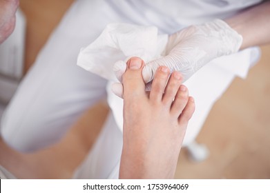 Pedicurist doing professional medical pedicure procedure in beauty salon with special instrument. Foot treatment in SPA salon. Podiatry clinic. Beautician doctor hands in white gloves with female legs