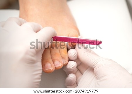 Pedicurist hands in protective rubber gloves filing toenails on feet with a nail file in a beauty salon