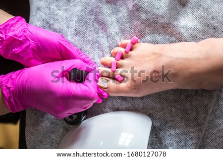 Pedicurist master in pink gloves cuts the cuticle and shellac toe nails in the pedicure salon using drill.  Professional pedicure in cosmetology clinic. Hygiene for feet in beauty salon.