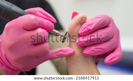 A pedicurist treats the toes of a client using a machine with an abrasive disc in a beauty salon.
